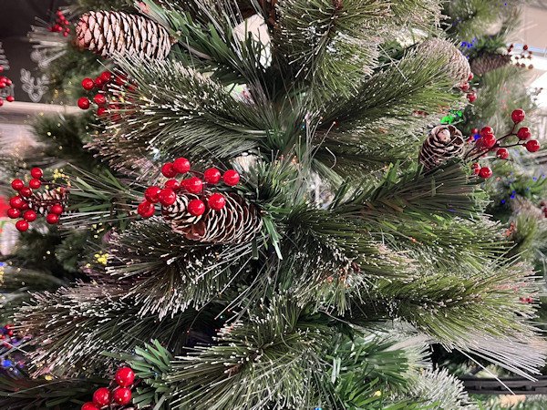 Close up of an artificial Christmas tree with frosted branches, fake pine cones and fake red berries